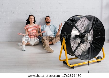 Happy couple sitting on floor near electric fan at home