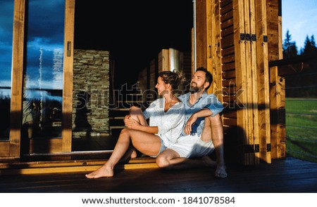 Happy couple sitting on patio of wooden cabin, holiday in nature concept.
