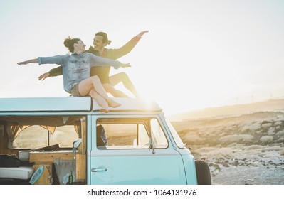 Happy couple sitting on top of minivan roof at sunset - Young people having fun on summer vacation traveling around the world - Travel, love, van lifestyle and freedom concept - Focus on bodies - Powered by Shutterstock