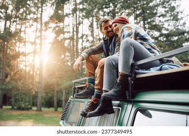 Happy couple sitting on top of their van while camping in the woods. - Powered by Shutterstock