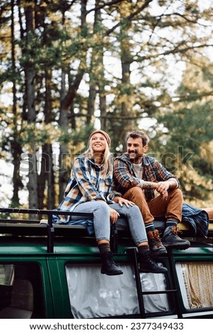 Happy couple sitting on top of their camper trailer while relaxing in nature. 