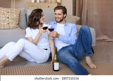 Happy couple sitting, relaxing on floor in living room, drinking red wine. Smiling young husband and wife rest at home enjoy romantic date on family weekend together - Powered by Shutterstock