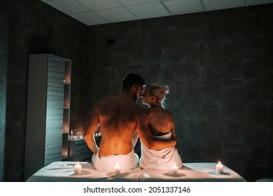 A happy couple is sitting together in the dark surrounded by candles and hugging in the massage room. They enjoying a weekend at the spa center. A couple at the spa center. Romantic weekend.