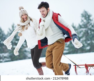 Happy Couple With Sled Running Through Snow In Winter