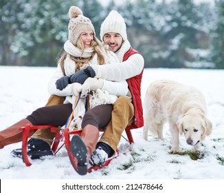 Happy Couple Sledding With Toboggan And Dog In Winter