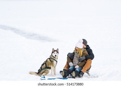 Happy Couple Sledding With Toboggan And Dog In Winter. Selective Focus In Dog.