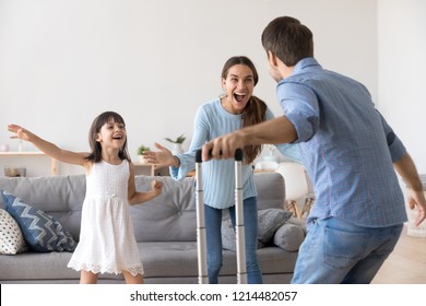 Happy couple and small daughter standing in living room at home. Cheerful wife little girl meets husband father he arrived at home with suitcase luggage from long business trip. Family reunion concept - Powered by Shutterstock