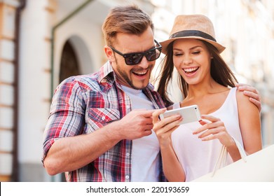 Happy Couple With Smart Phone. Happy Young Loving Couple Standing Outdoors Together And Looking At The Mobile Phone Together