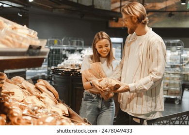 Happy couple smiles while choosing fresh bread at a grocery store bakery, enjoying a simple moment of togetherness in their modern, cheerful shopping experience - Powered by Shutterstock