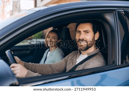 Happy couple smiling at the camera while driving a modern electric car on a road trip, enjoying leisure time together and sharing a joyful, adventurous journey with seatbelts fastened