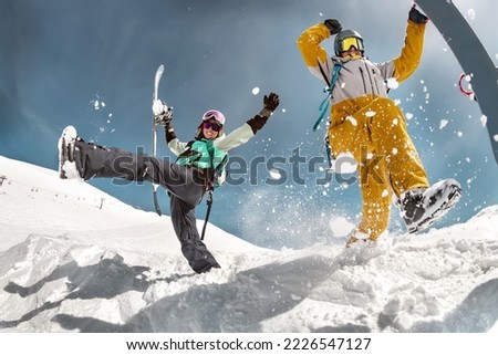 Happy couple of snowboarders are having fun and jumps with snowboards in hands. Winter holidays at ski resort