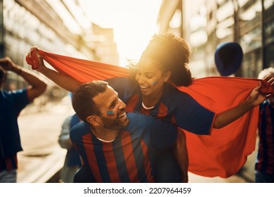 Happy Couple Of Soccer Fans Piggybacking While Celebrating Victory Of Their Favorite Team On The Street.