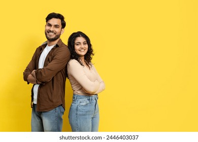 Happy couple standing back to back with confident smiles, dressed casually against a vibrant yellow background - Powered by Shutterstock