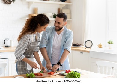 Happy couple standing in kitchen at home preparing together yummy dinner on first dating, spouses chatting enjoy warm conversation and cooking process, caring for health, eating fresh vegetable salad