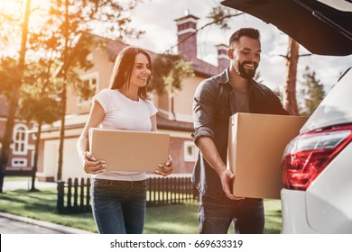 Happy Couple Is Standing Near Car With Cardboard Boxes. Moving Day.