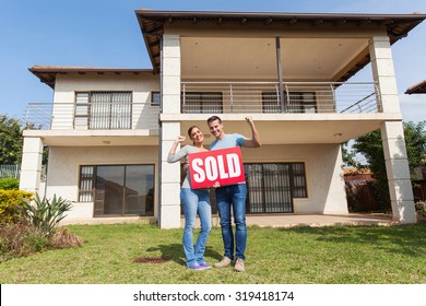 happy couple standing outside their house and holding sold sign