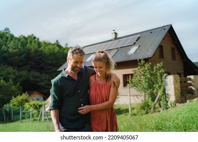 Happy couple standying near their house with solar panels. Alternative energy, saving resources and sustainable lifestyle concept.