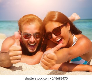 Happy Couple In Sunglasses Having Fun On The Beach. Summer Vacation. Laughing Family Enjoying Nature Over Sea Background. Attractive Man And Woman At The Beach 