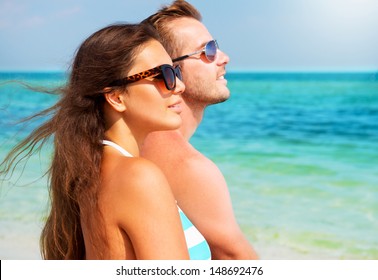 Happy Couple In Sunglasses Having Fun On The Beach. Summer Vacation. Laughing Family Enjoying Nature Over Sea Background. Attractive Man And Woman At The Beach 