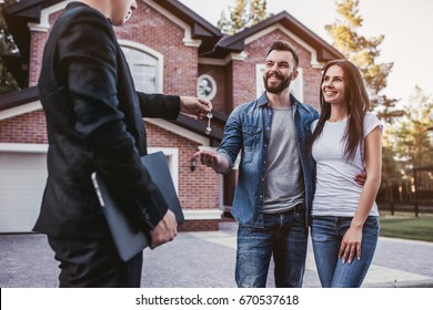 Happy couple is taking keys from their new house from broker and smiling. - Shutterstock ID 670537618