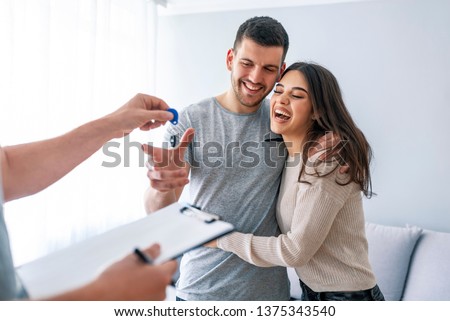 Happy couple is taking keys from their new house from broker and smiling. Hands of estate agent giving keys to the couple. The agent handed the keys a young couple
