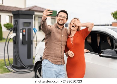 Happy Couple Taking Selfie At Electric Car Charging Station. Eco-Friendly, Sustainable Transportation, Technology. - Powered by Shutterstock