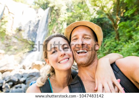 Happy couple taking selfie portrait at tropical waterfalls in summer vacation