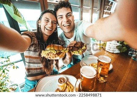 Happy couple taking selfie with smart mobile phone at burger pub restaurant - Young people having lunch break at cafe bar venue - Life style concept with guy and girl hanging out on weekend day 