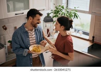 Happy couple talking while drinking wine and eating spaghetti in the kitchen. 
