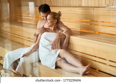 Happy couple talking while sitting close to each other in sauna at health spa.  The view is through the glass.  - Powered by Shutterstock