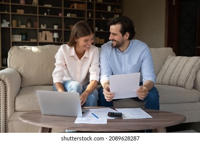 Happy couple of tenants, homeowners doing domestic paperwork, reading paper documents, using laptop computer, calculating expenses, paying bills, insurance, mortgage fees on internet with online app