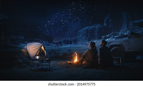 Happy Couple Tent Camping in the Canyon, Sitting by Campfire Watching Night Sky with Milky Way Full of Bright Stars. Two Travelers In Love On a Romantic Vacation Trip. Back View Shot - Powered by Shutterstock