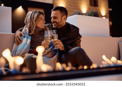 Happy couple toasting with wine while enjoying in romantic evening by fireplace on a patio. - Powered by Shutterstock