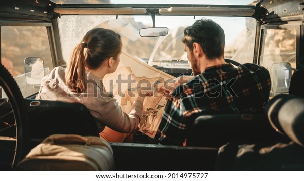 Happy Couple of Tourists Choosing Path with a Map\
while Driving Off Road SUV, Riding Through the Desert Canyon.\
Adventurous Travelers Having Fun, Exploring Mountains. Marvelous\
Nature. Back View Shot