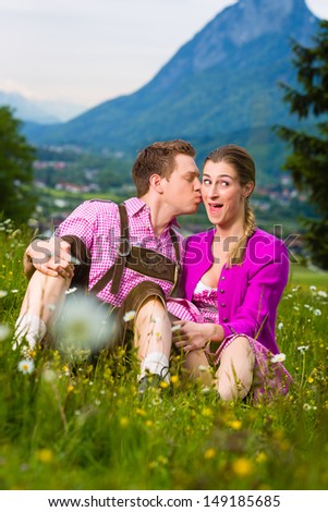 Happy Couple in traditional dress sitting in the meadow with mountain panorama