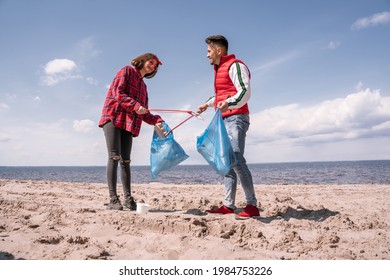 Happy Couple With Trash Bags And Grabbers Picking Up Garbage On Sand 