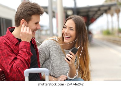 Happy couple of travelers sharing music on holidays during a travel in a train station - Powered by Shutterstock