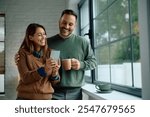 Happy couple using app on mobile phone by the window. Copy space. 