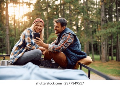 Happy couple using cell phone while relaxing on roof of their camper trailer in the woods. Copy space.  - Powered by Shutterstock