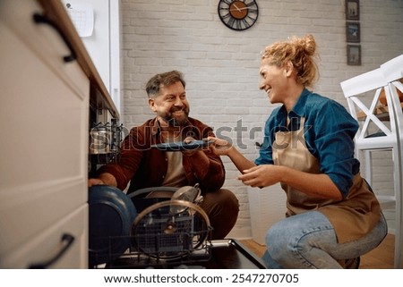 Happy couple using dishwasher in the kitchen.
