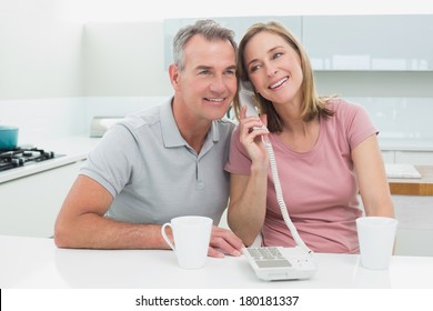 Happy Couple Using Landline Phone Together In The Kitchen At Home