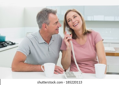 Happy Couple Using Landline Phone In The Kitchen At Home