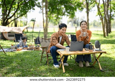 Happy couple using laptop while camping with their daughter in the background