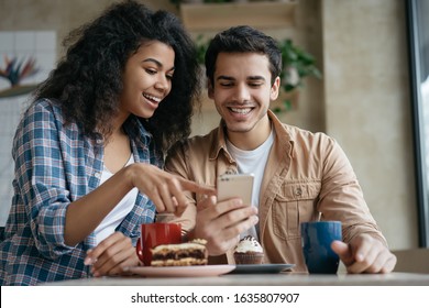 Happy couple using mobile phone application for online shopping. Emotional friends communication, laughing, looking at digital screen, sitting together in cafe 