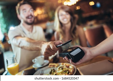 Happy couple using mobile phone and making contactless payment in a restaurant. S - Powered by Shutterstock