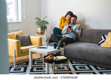 Happy couple using mobile phone at home stock photo - Powered by Shutterstock