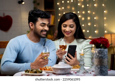 Happy couple using mobile phone while having drinks during romantic candlelight dinner - concept of wedding anniversary celebration, bonding and dating application - Powered by Shutterstock