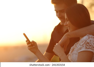 Happy couple using a smartphone in a sunset back light on the beach - Powered by Shutterstock