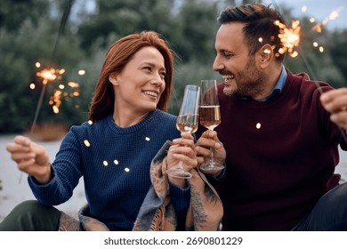 Happy couple using sparklers while toasting with champagne during autumn day outdoors.
