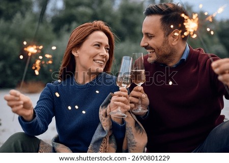 Happy couple using sparklers while toasting with champagne during autumn day outdoors.